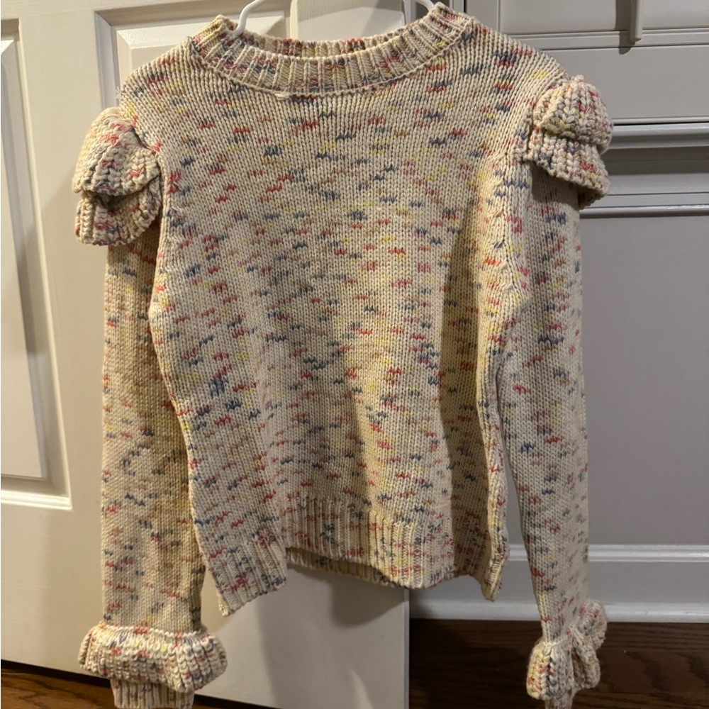 White sweater with different colors on it and ruffled sleeves